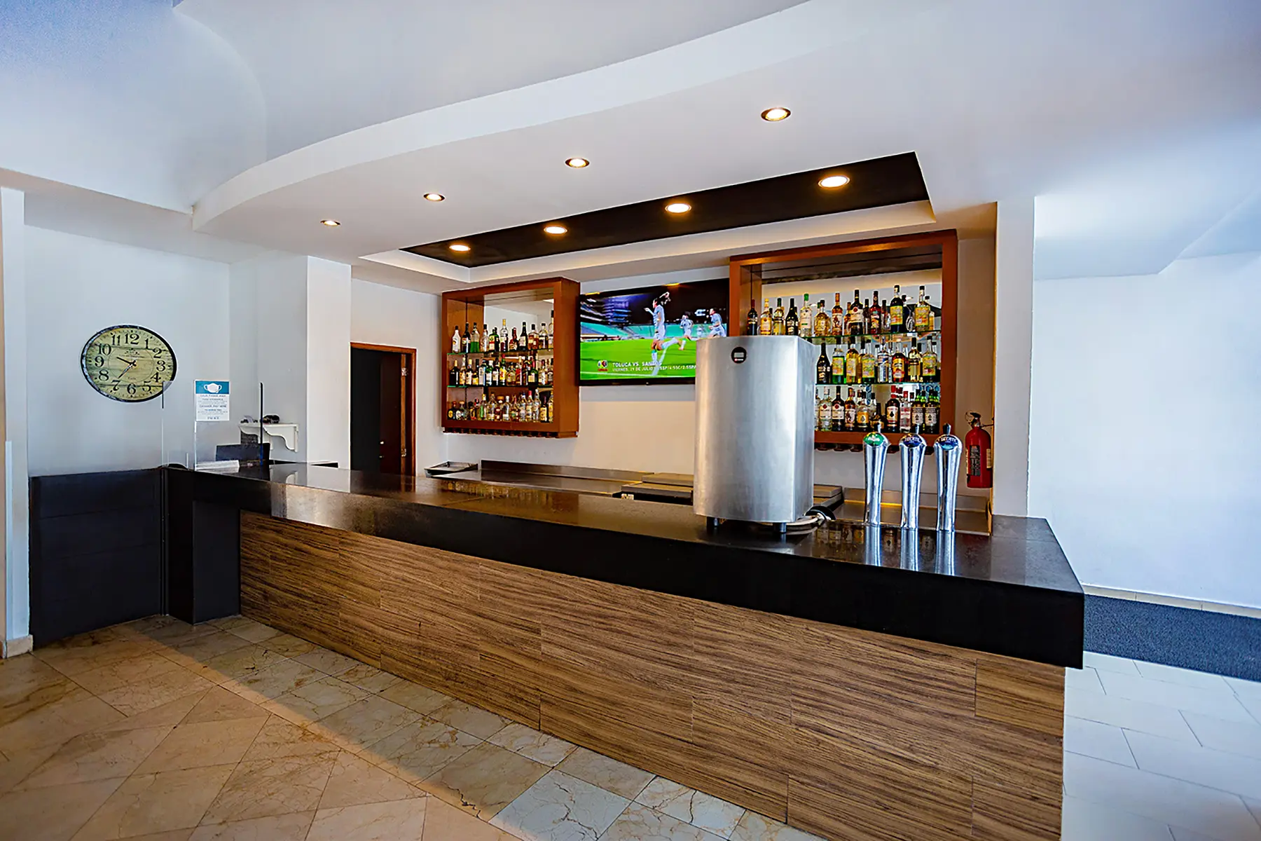 Wooden drinks bar, a clock, bottles of alcohol and a screen in Grand Central Sport Bar at the Oceano Palace Mazatlán hotel